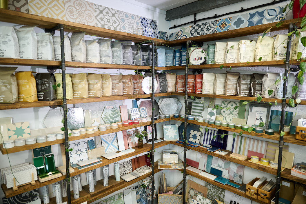 Shelving at The Bathroom Studio showroom in Goring-on-Thames, displaying a curated selection of Ca Pietra tile samples alongside grout colours, paint samples, and decorative accessories.